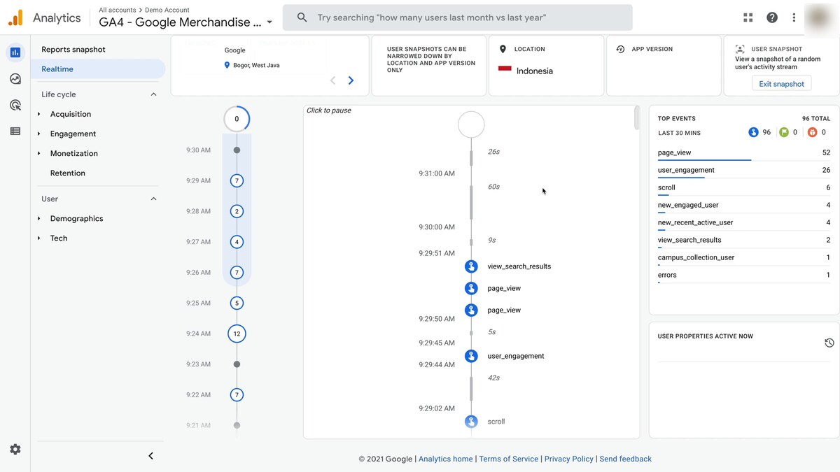 Google Analytics 4 Realtime view on the public Demo Account / Google Merchandise Store — left rail with Reports snapshot, Realtime (active), Life cycle / Acquisition / Engagement / Monetization / Retention / User / Demographics / Tech, a User Snapshot panel showing one user's activity stream from 9:21 to 9:31 AM with view_search_results, page_view, and user_engagement events at each timestamp, USER SNAPSHOTS / LOCATION (Indonesia) / APP VERSION filters, a Top Events leaderboard (page_view 52, user_engagement 26, scroll 6, new_engaged_user 4, errors 1), and Click to pause control